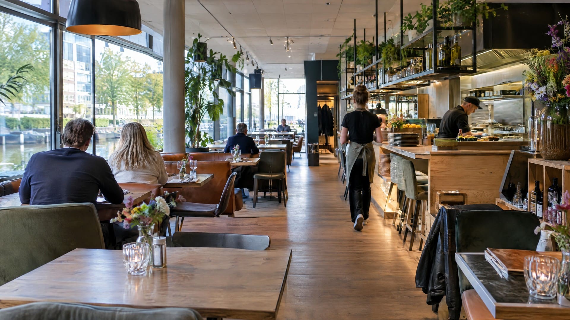 Restaurantzaal met open keuken, houten tafels en hoge ramen